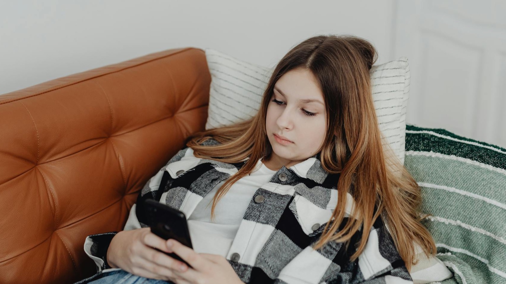 Teen girl lying on sofa using smartphone, enjoying casual indoor relaxation.