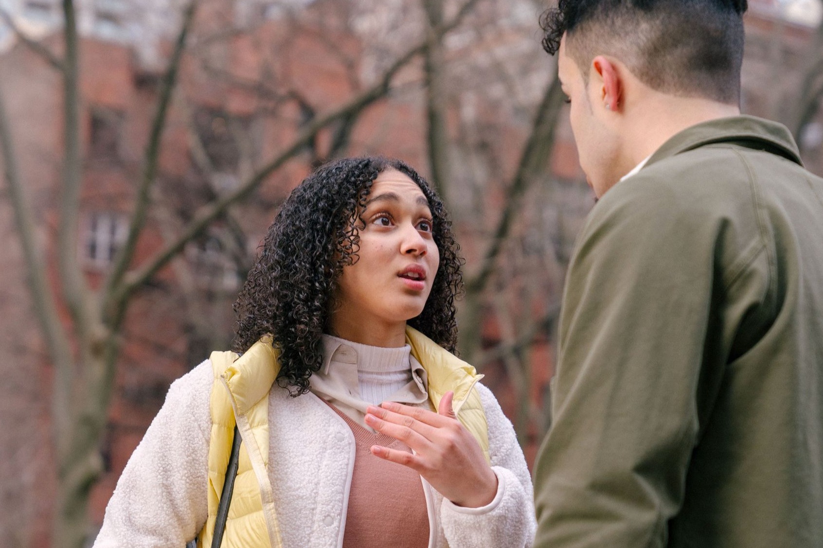 Ethnic female with short curly hair standing and arguing with boyfriend on street in daylight